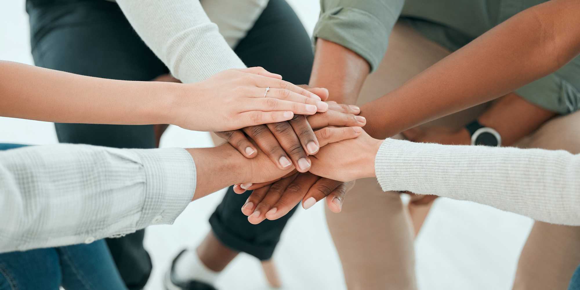 Multicultural people gathered in a circle with their hands stacked together showing unity.